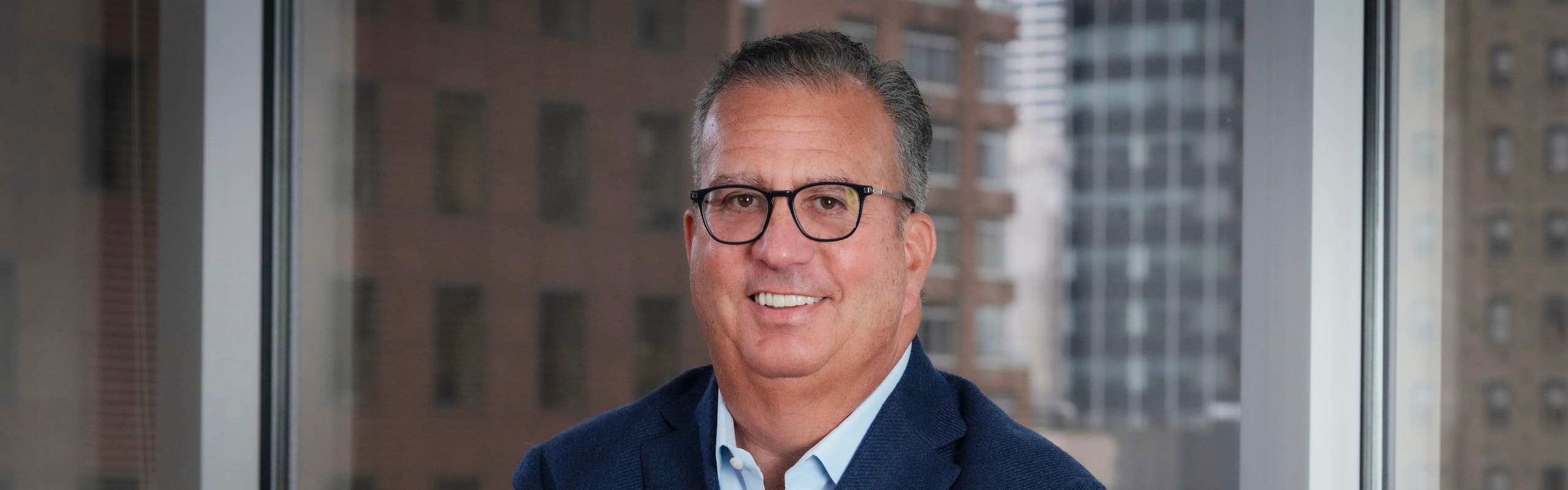 eadshot of the CEO, Steven Millner, in a navy jacket, standing in front of an office window.
