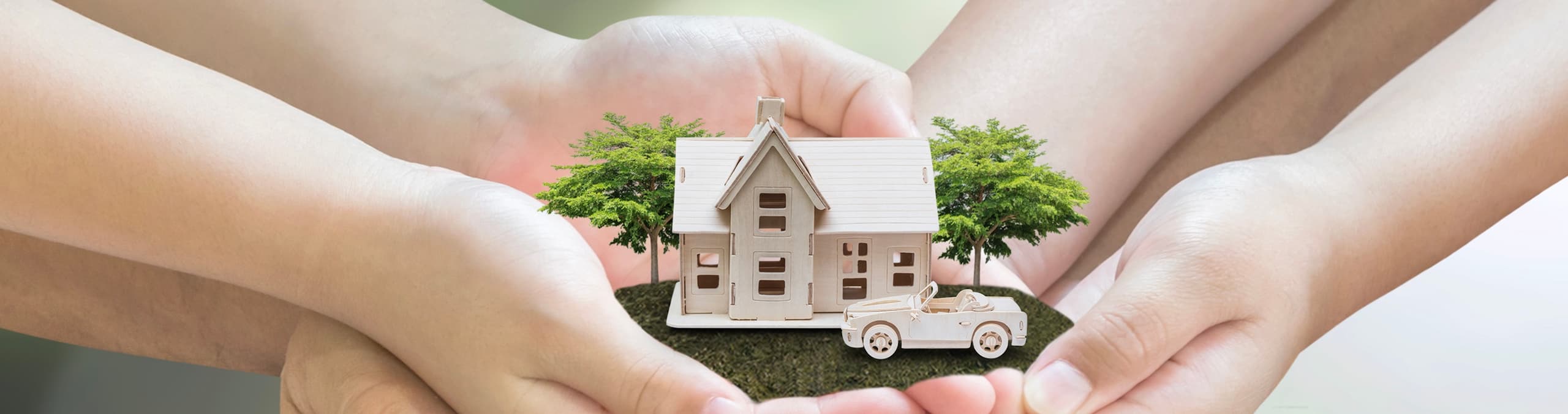 An adult's hands holding a miniature toy house model alongside a child's hands on a white background, representing family homeownership.