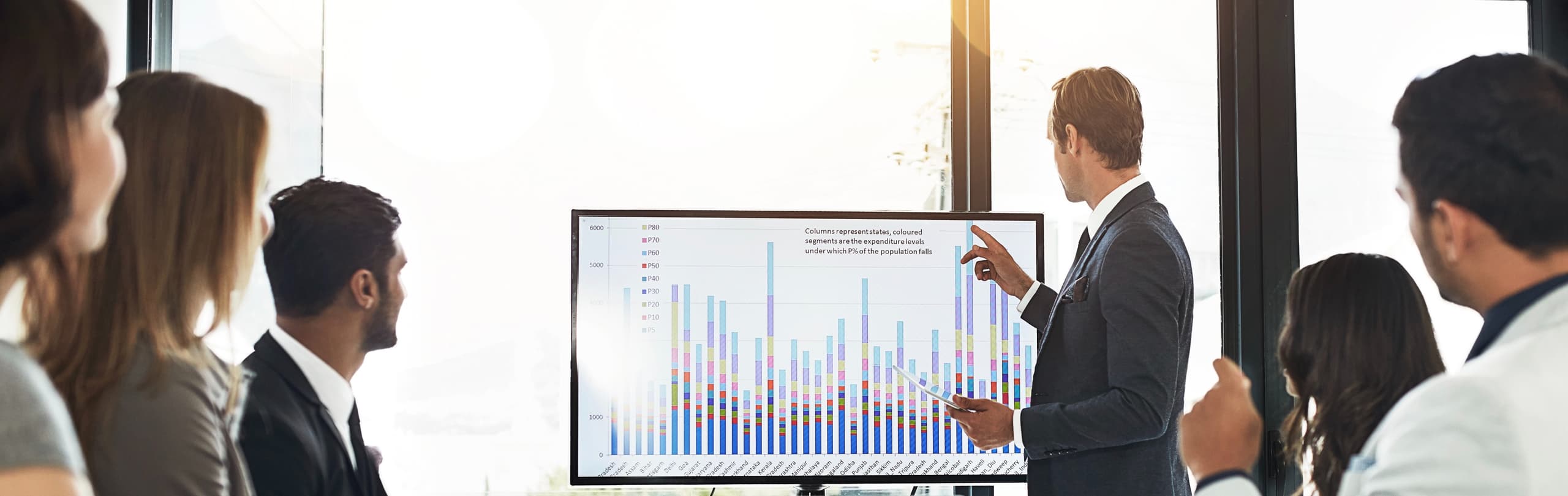A businessman pointing at a presentation screen while presenting to his team.