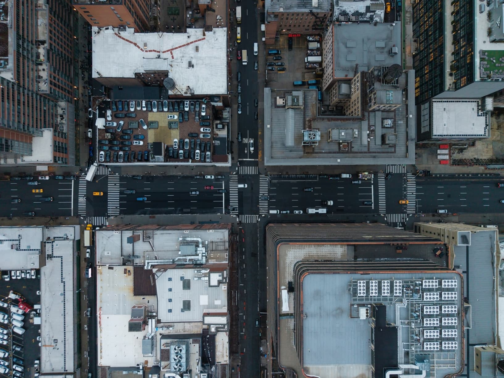Aerial view of a four-way city street intersection surrounded by rooftops and buildings.