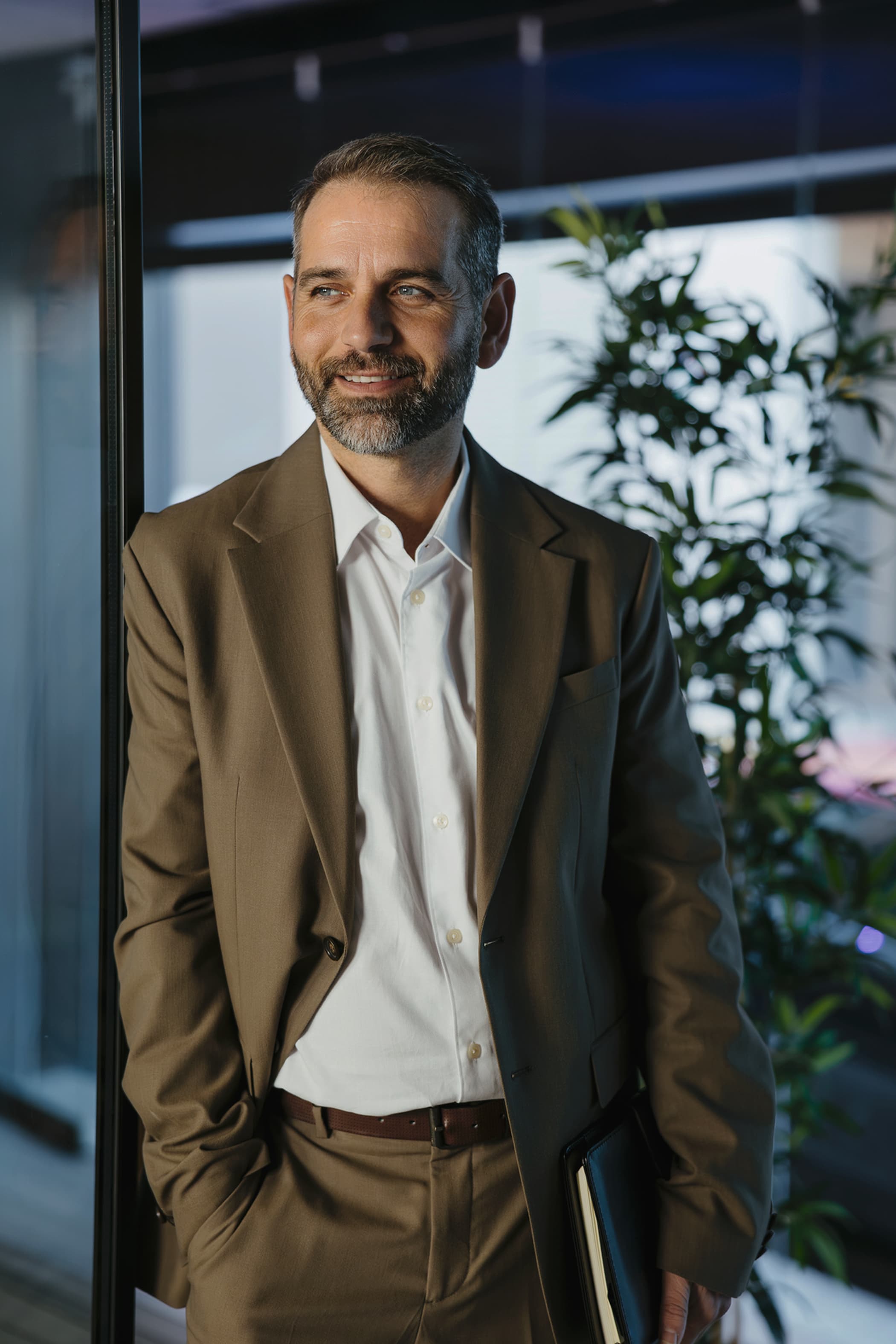 Portrait photo of a smiling man in a suit leaning against a glass partition.