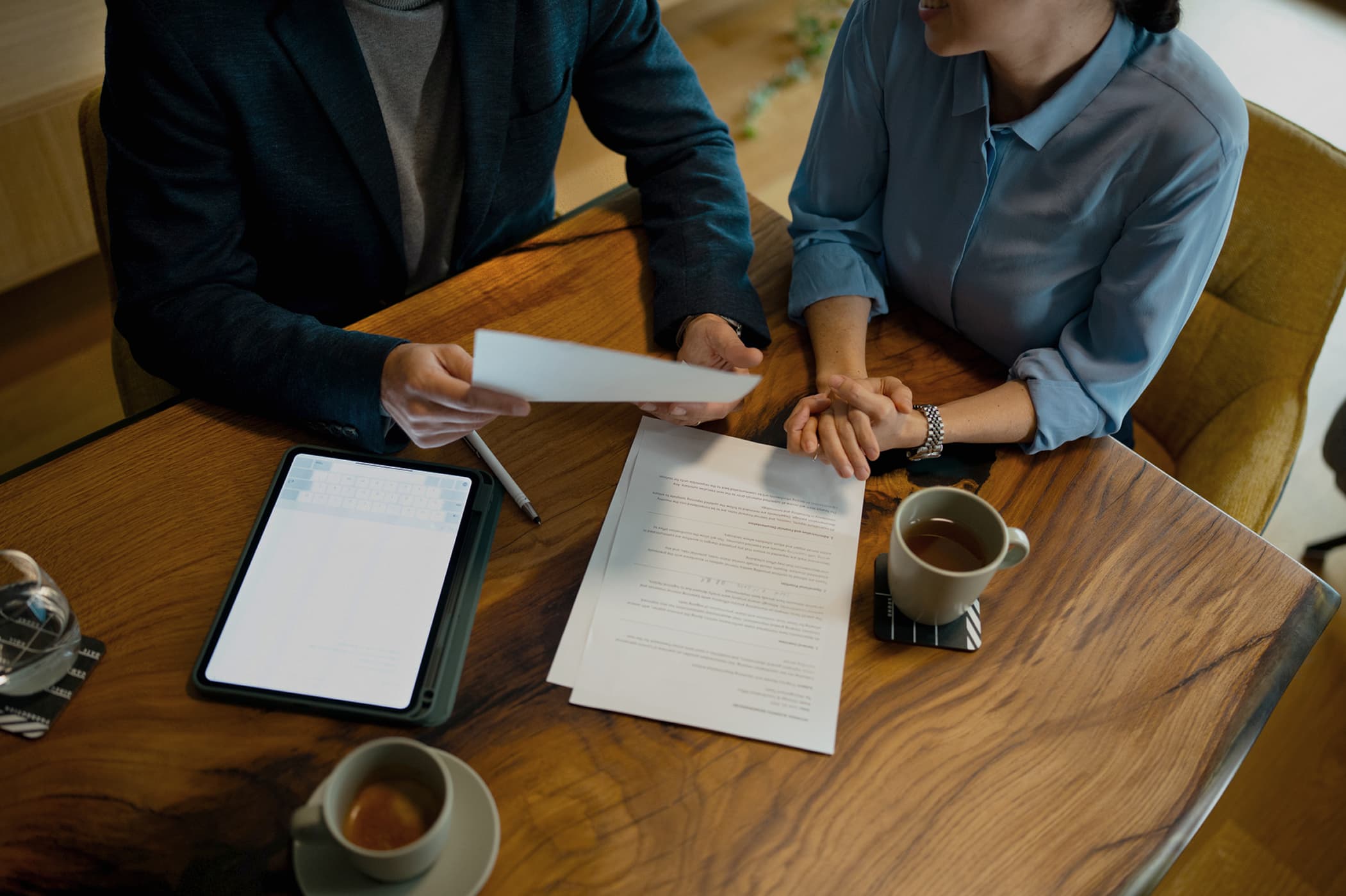 Top view of a consultant and a client discussing business at a wooden table with papers in front of them.
