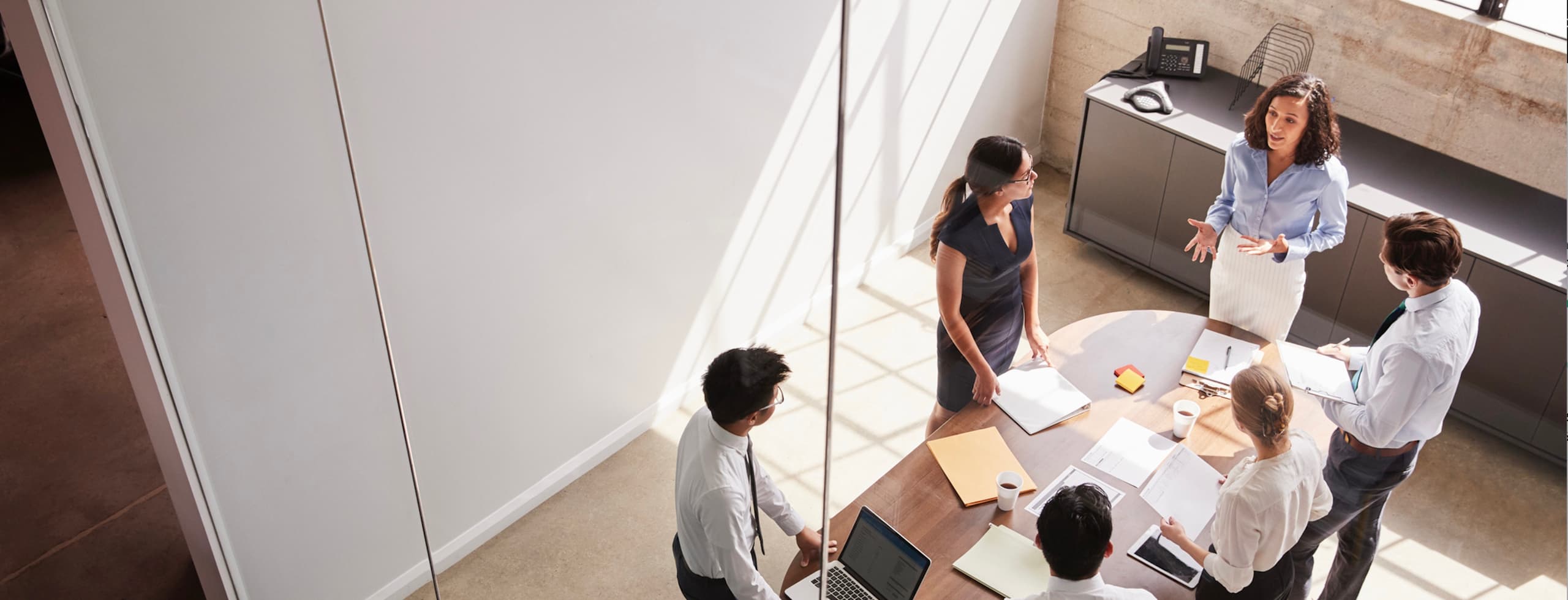 An elevated view of a diverse group of corporate professionals collaborating around a light-colored round table in a bright office.