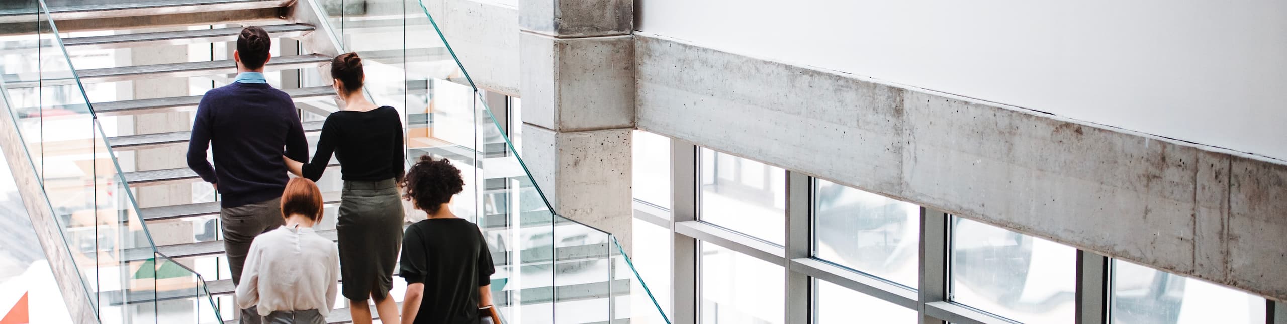 A view of several professionals walking up a modern glass and concrete staircase inside a bright office building.