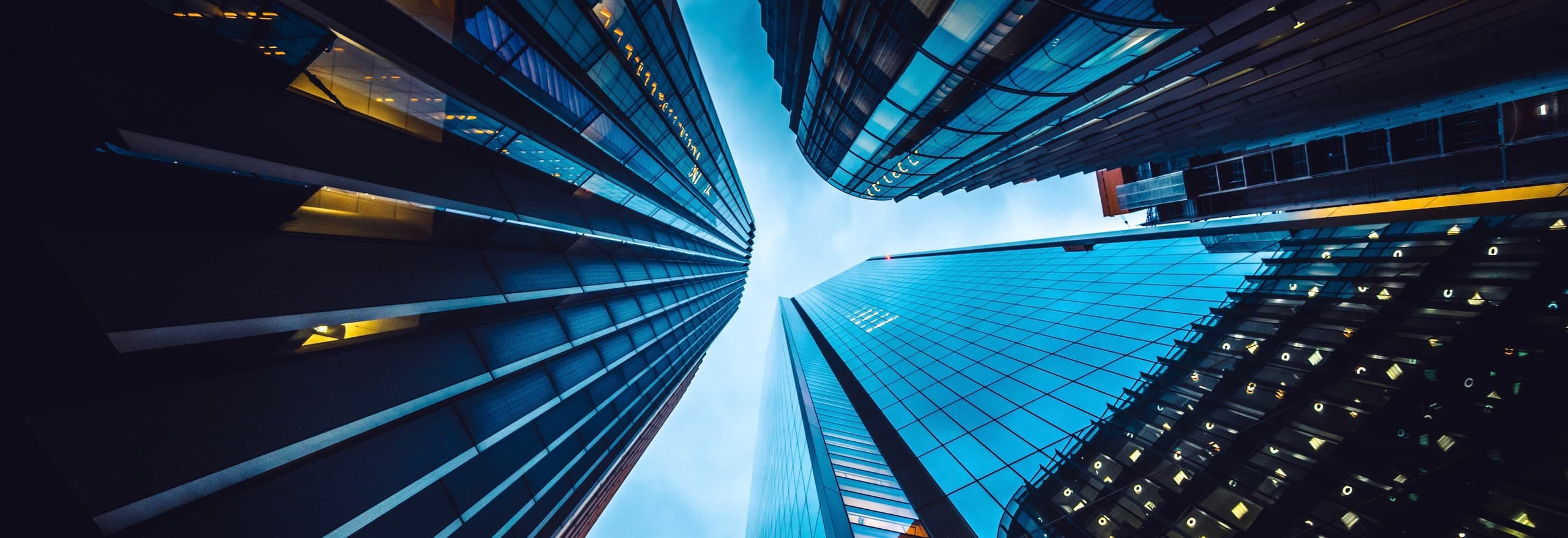 A low-angle view looking straight up at towering modern glass skyscrapers converging under a dark sky.