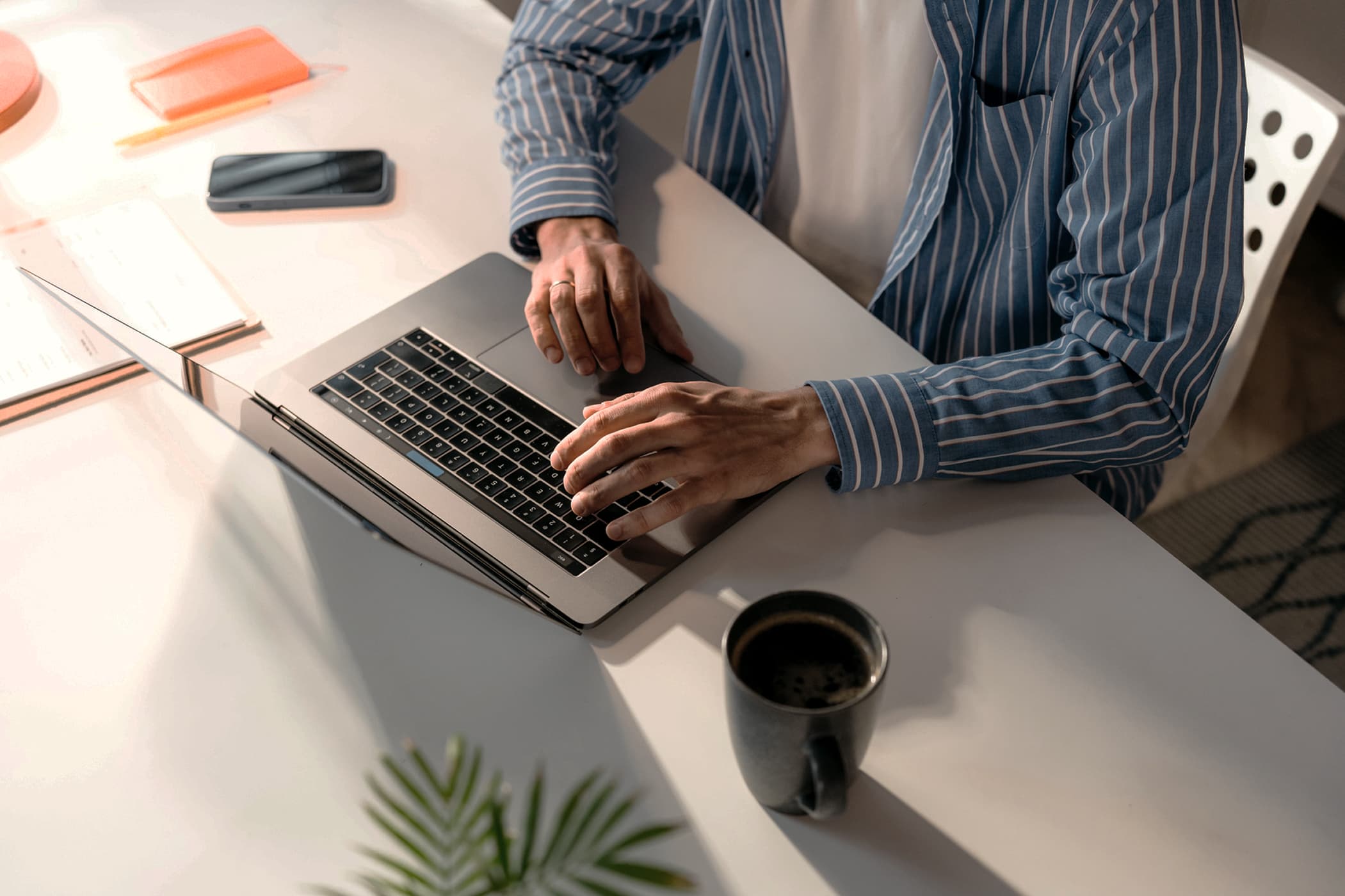 Hands typing on a laptop at a desk next to a cup of coffee.