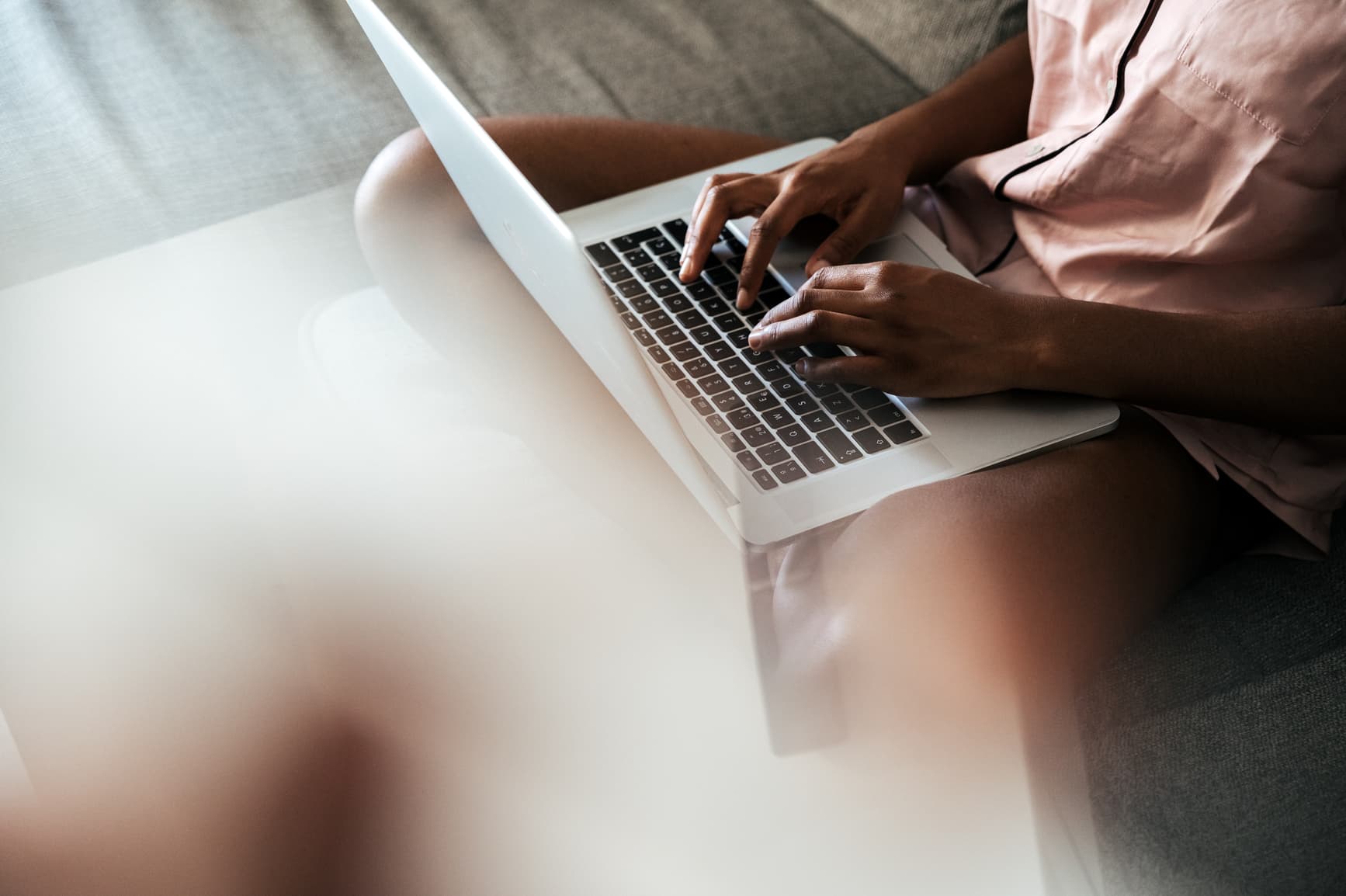 Close up of a woman typing on her laptop that is on her lap.