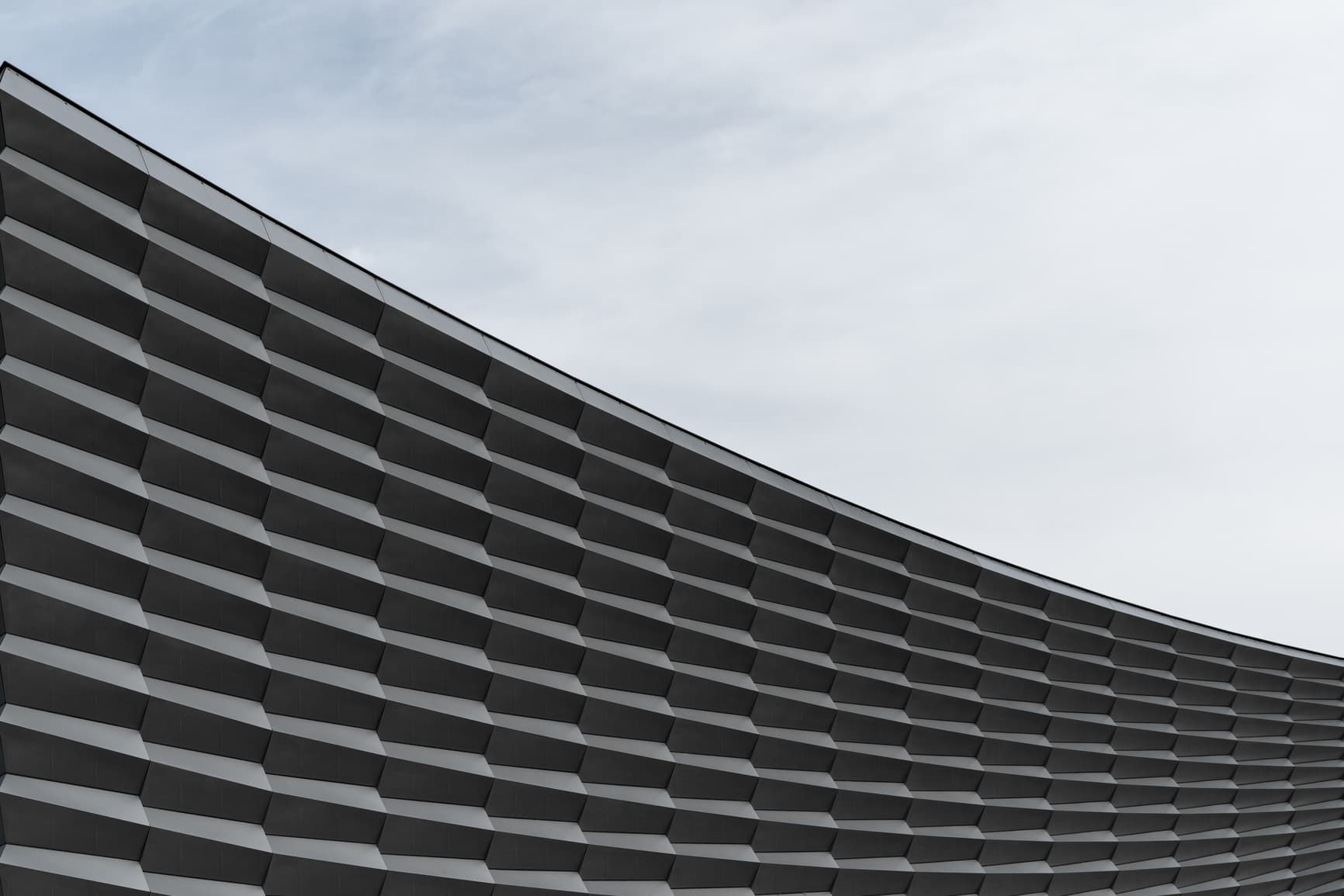 Low-angle view of a modern building's curved facade with repeating horizontal panels against a pale sky.