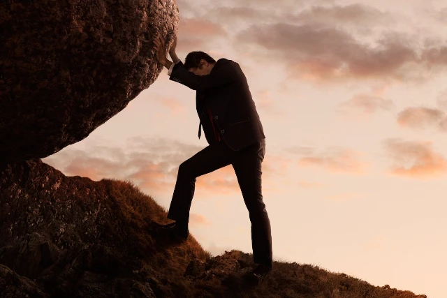 Man pushing boulder up a hill